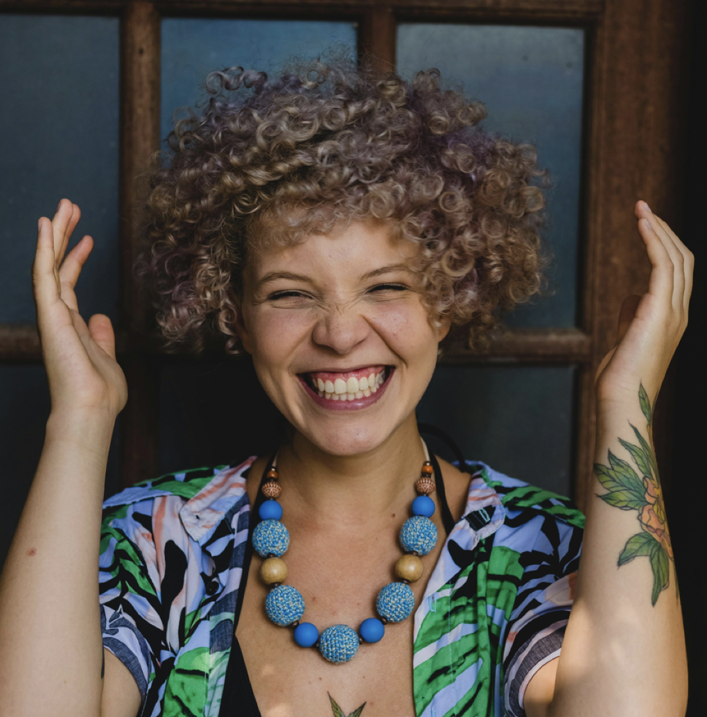 Jeune femme rayonnant et joyeuse avec une chemise ouvert aux motifs végétaux colorés, avec un collier de perles bleues pour illustrée le soins "Regain de vitalité