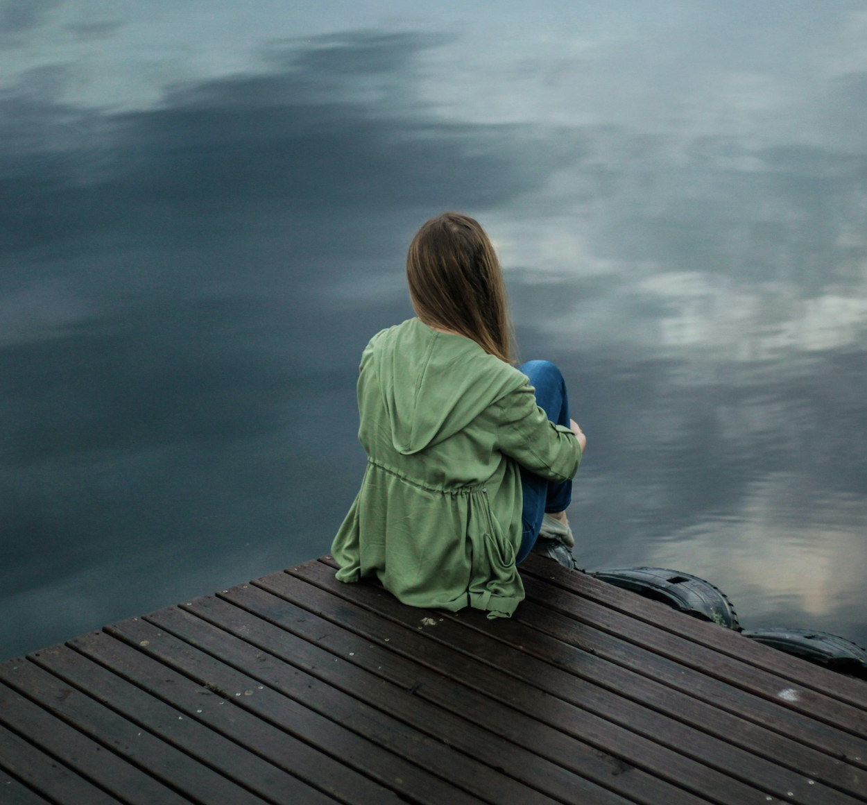 Jeune femme de dos assis au bord d'un lac, ambiance bleu et vert plutôt mélancolique qui illustre le soin "Ecueil de vie"